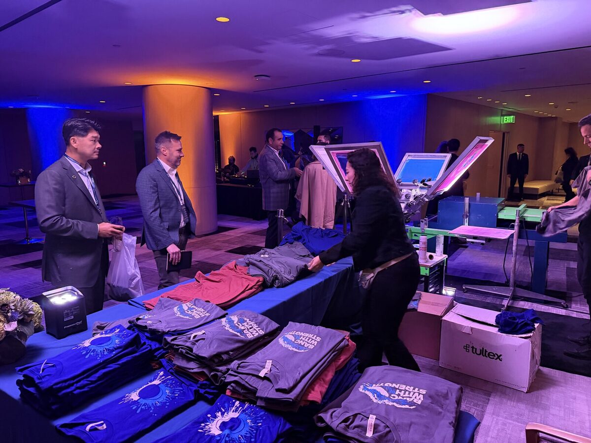Folded custom apparel arranged on tables at a corporate evening event with attendees in business attire