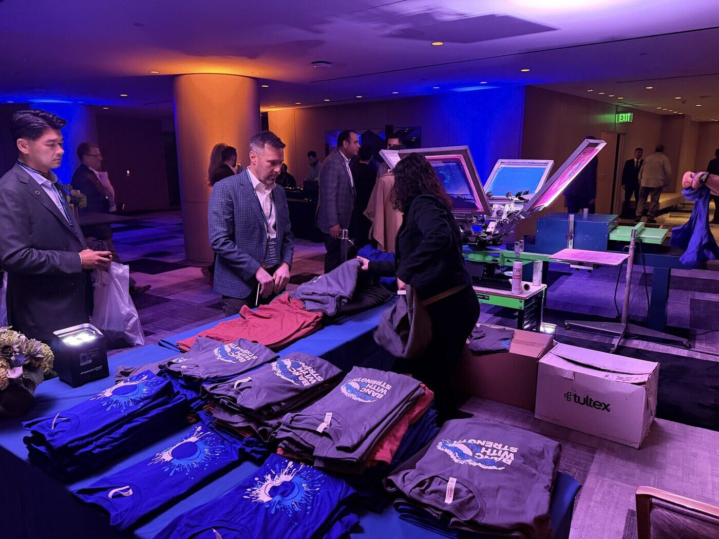 Personalization station with stacked apparel at a corporate reception with guests in suits