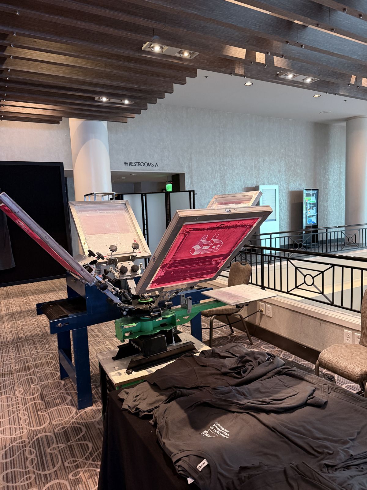 Personalization equipment and folded dark garments set up on a hotel mezzanine overlooking the lobby